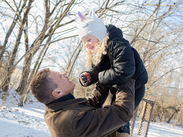 Man lifting up a girl with both hands, both wearing winter coats in a snow covered field