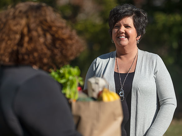 Woman smiling, standing in front of a person holding groceries