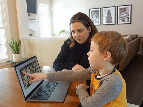 Woman and boy looking at a laptop screen that the boy is pointing to in a dining room
