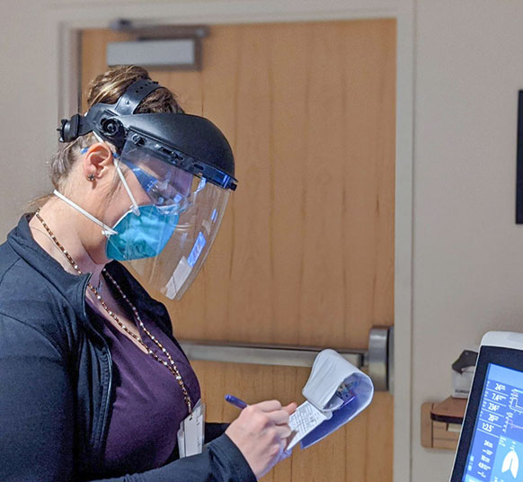 Woman with a face mask looking at a screen monitor while taking notes in her pad