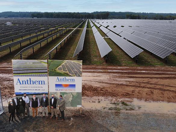 Group of people standing in front of a field with solar panels and an Anthem billboard