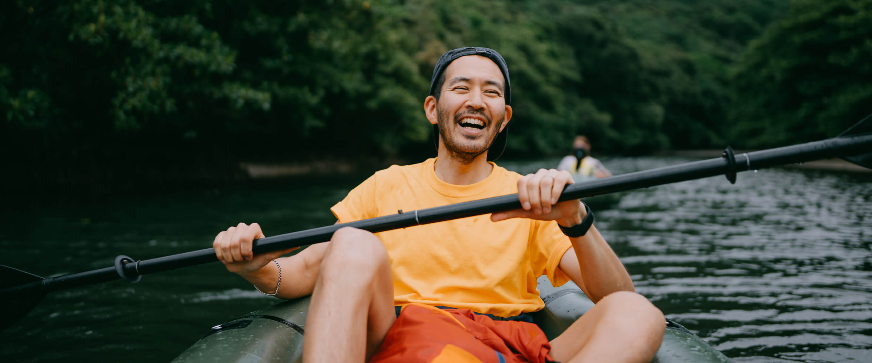 A man wearing an orange t-shirt smiling on a kayak holding a paddle on water.