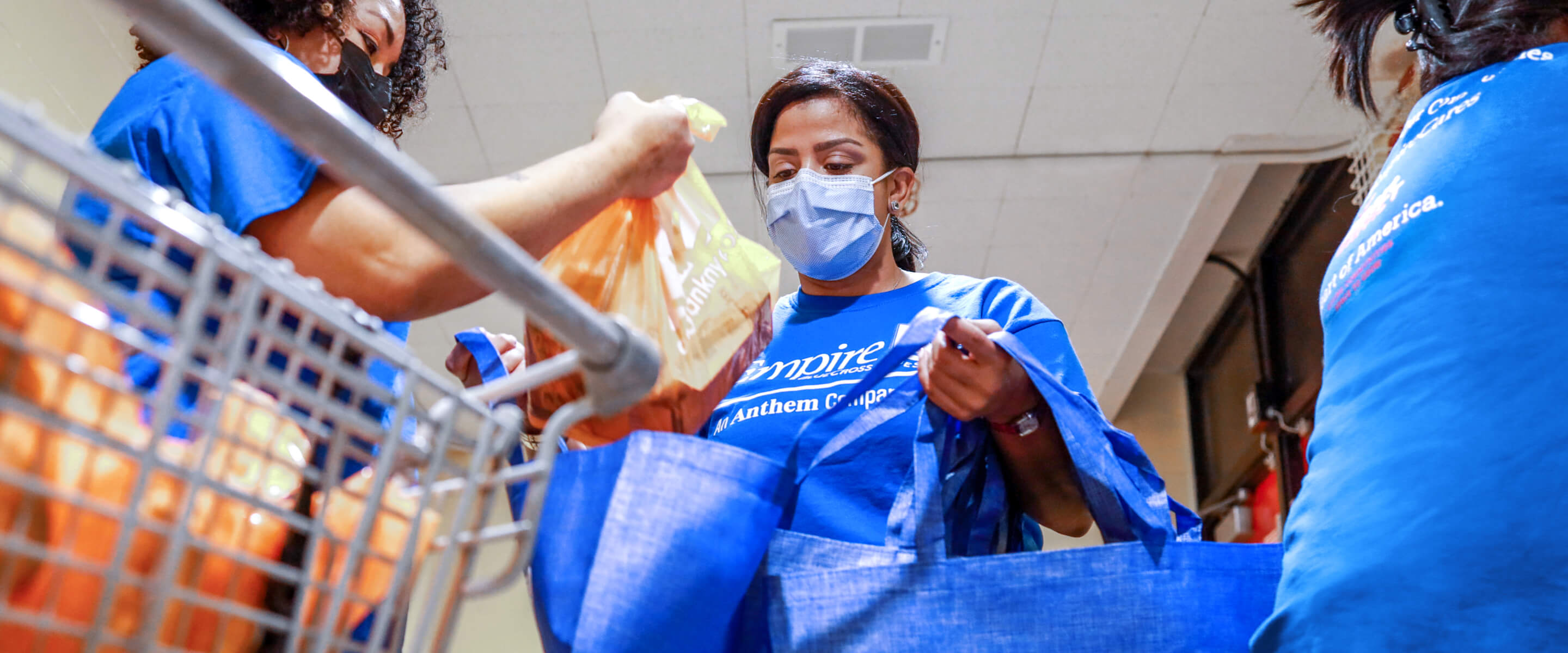 Two people wearing blue masks in blue t-shirts holding grocery bags.