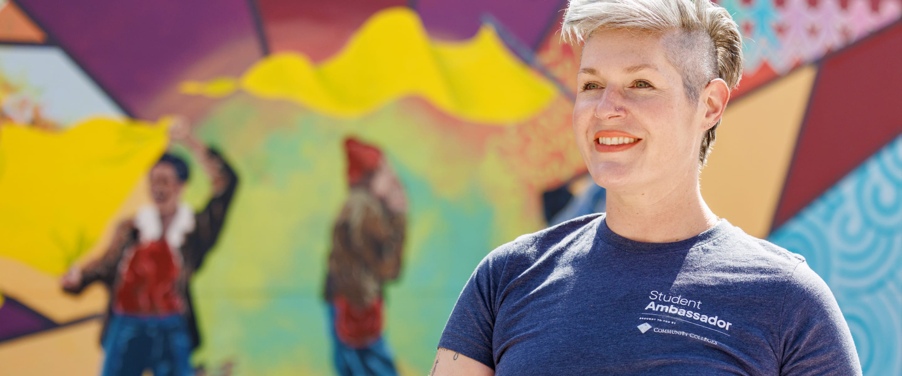 A person with short blonde hair wearing a dark t-shirt smiling.